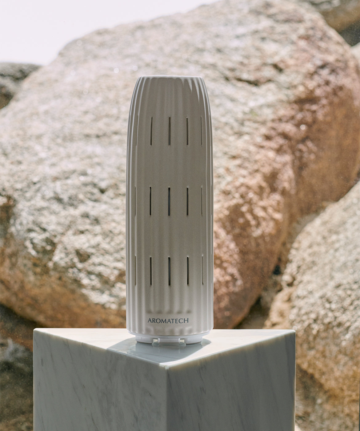 Ambience diffuser by Aromatech on a reflective white table with rocks in the background.