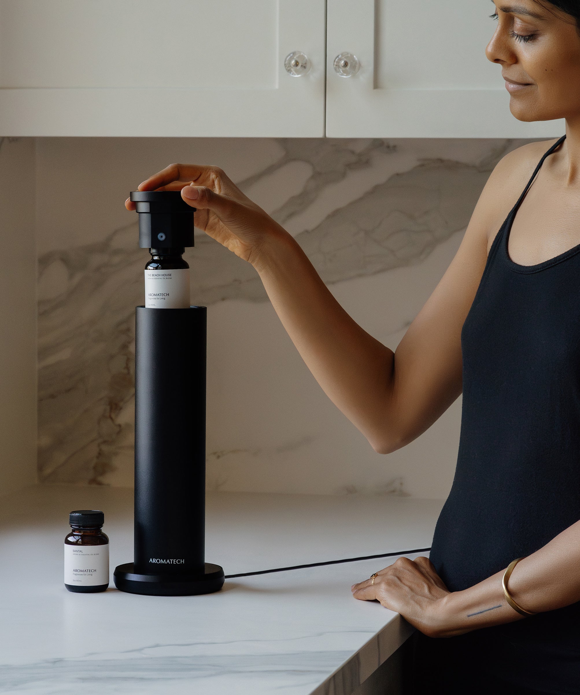 Woman inserting oil bottle into Aromini BT Plus diffuser on marble countertop