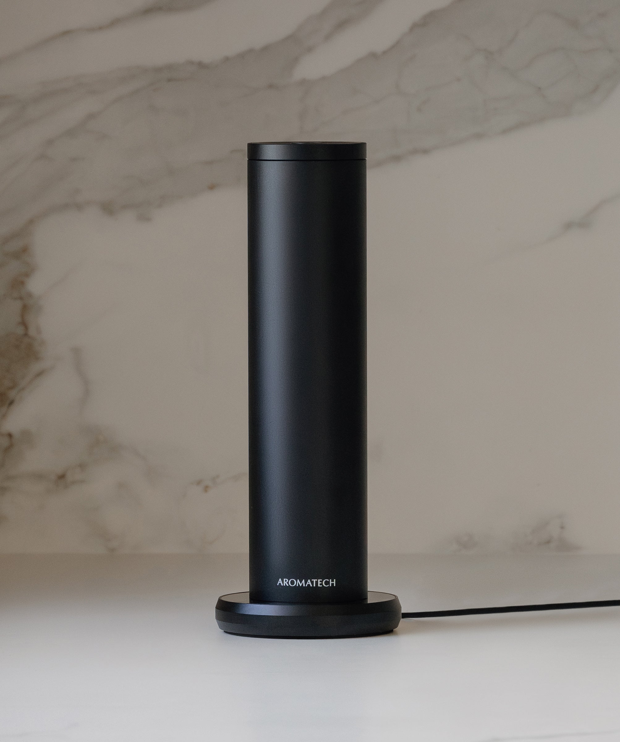 Sleek black AromaTech Aromini BT Plus diffuser against a modern marble backdrop