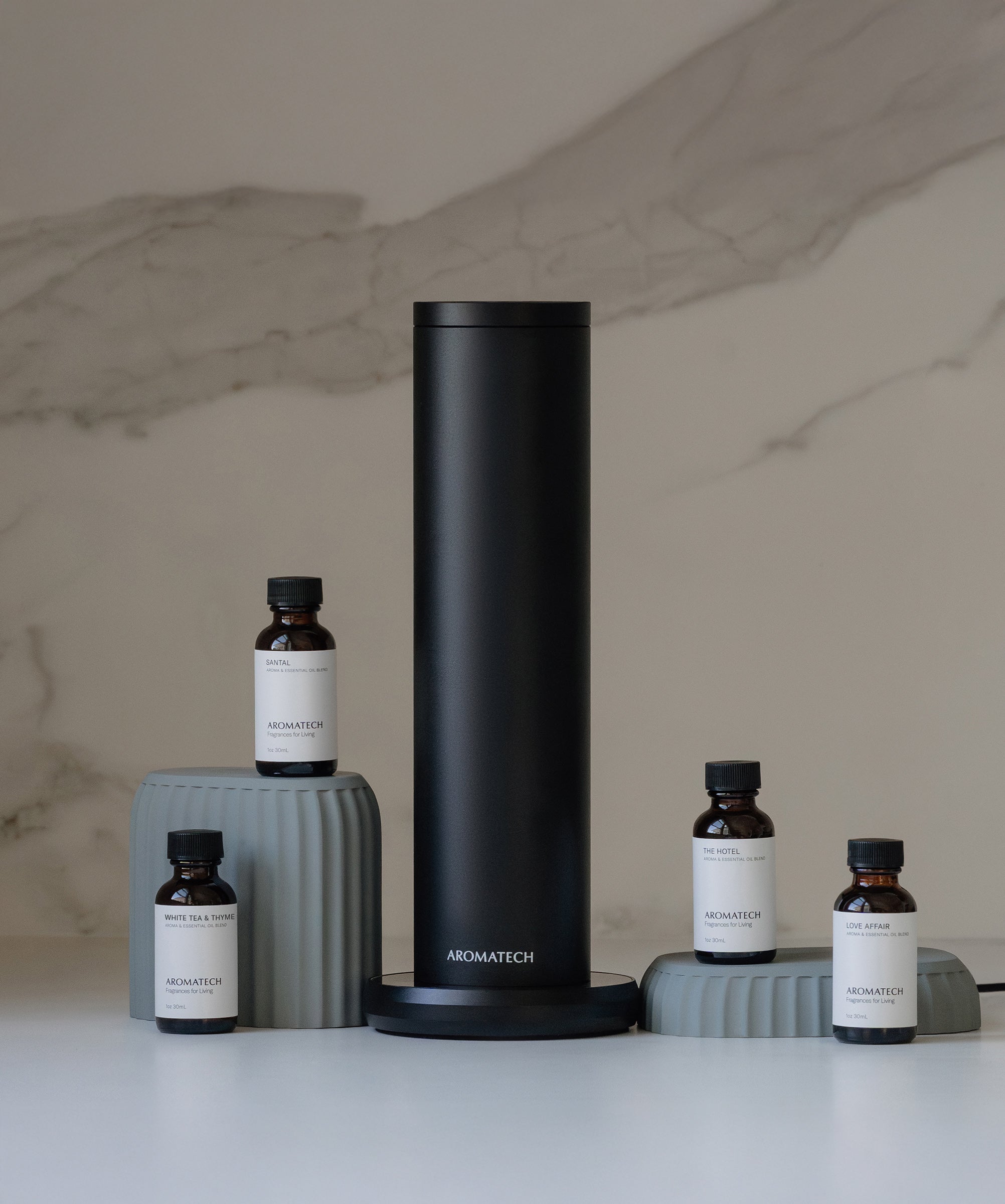 Aromatech AroMini BT scent diffuser with four fragrance oil bottles on a marble countertop